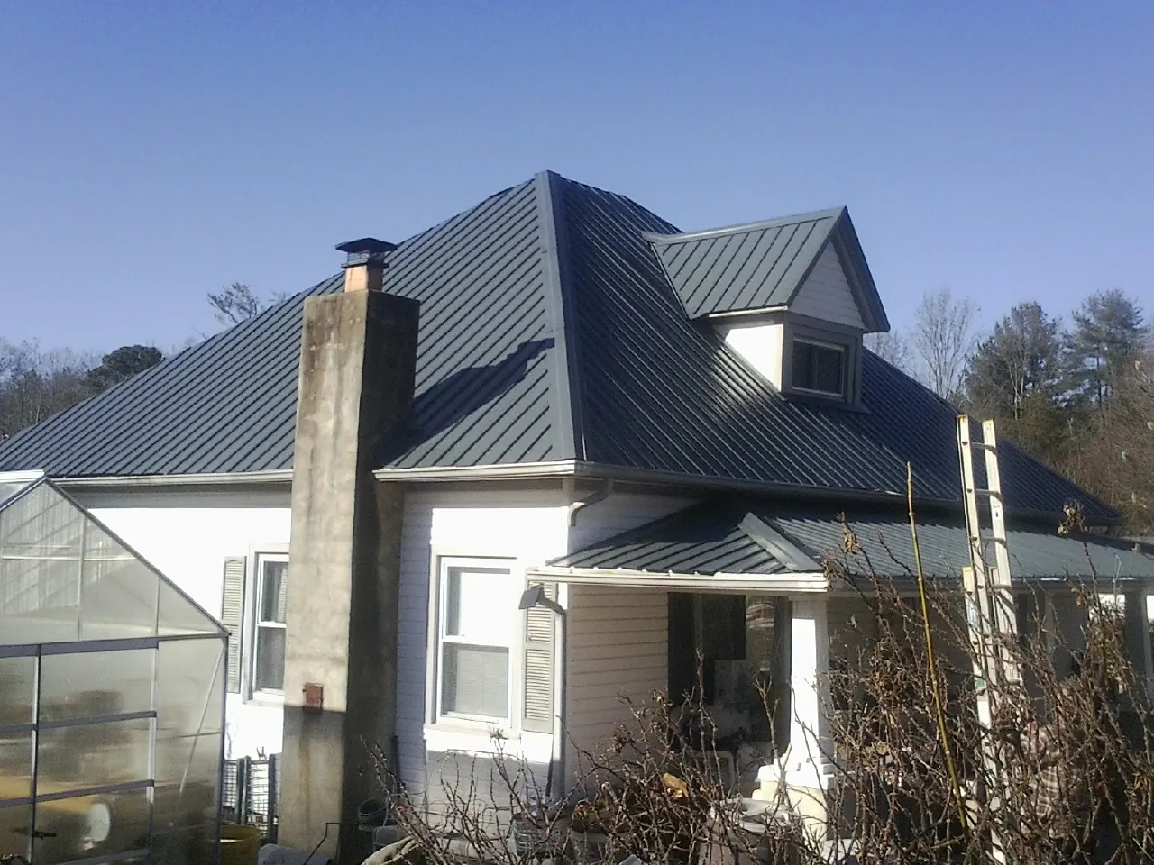 Dark blue standing seam metal roof on a white farmhouse with dormer — Slate & Tile Roof Repair by Roofing Brothers in Staples