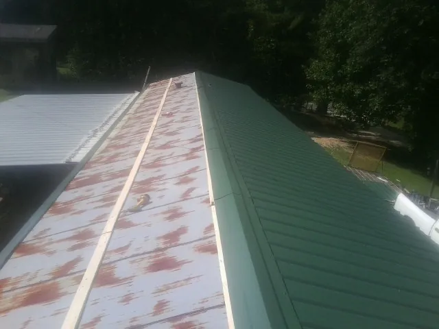 Old rusted panels beside newly installed green metal roofing — Wind Damage Roof Repair by Roofing Brothers in Staples