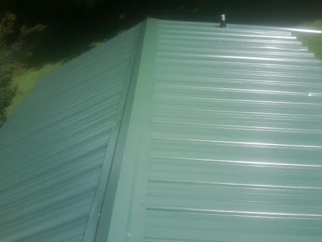New green metal panels meeting at the ridge of a roof — Flat Roof Repair work by our crew in Staples