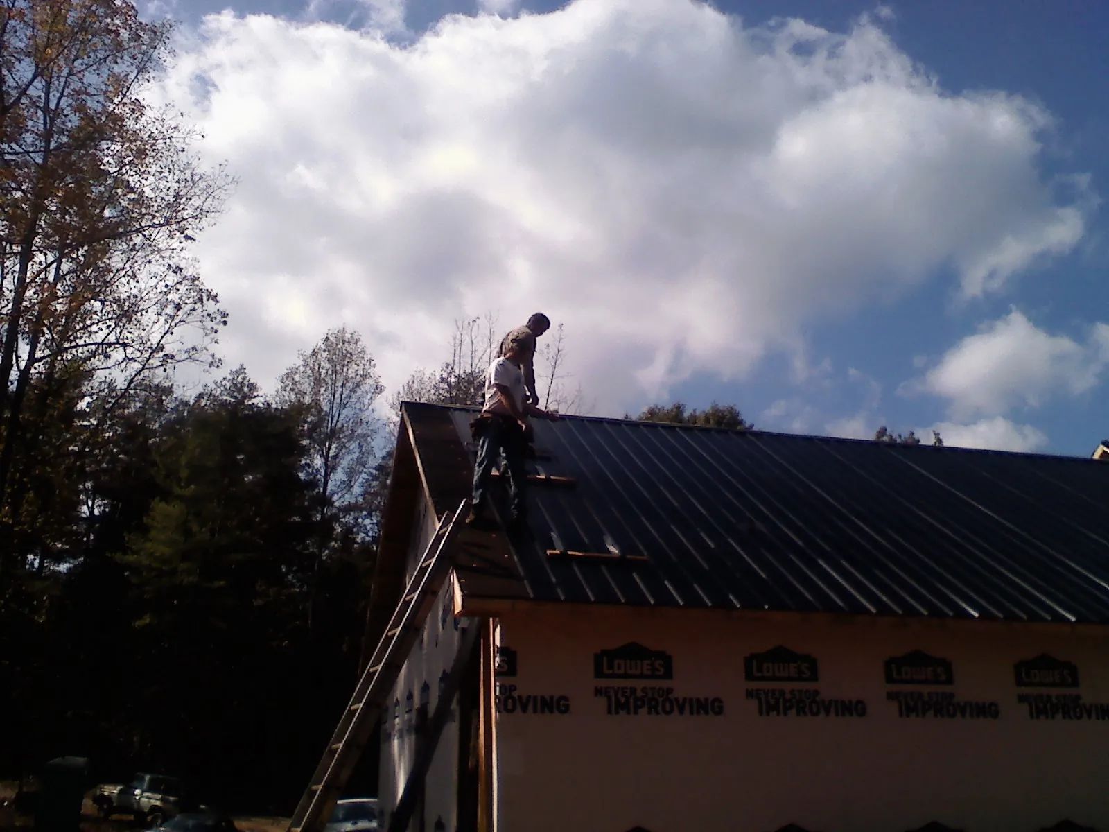 Roofer fastening dark metal panels high against a cloudy sky, from a Roof Inspection job in Staples