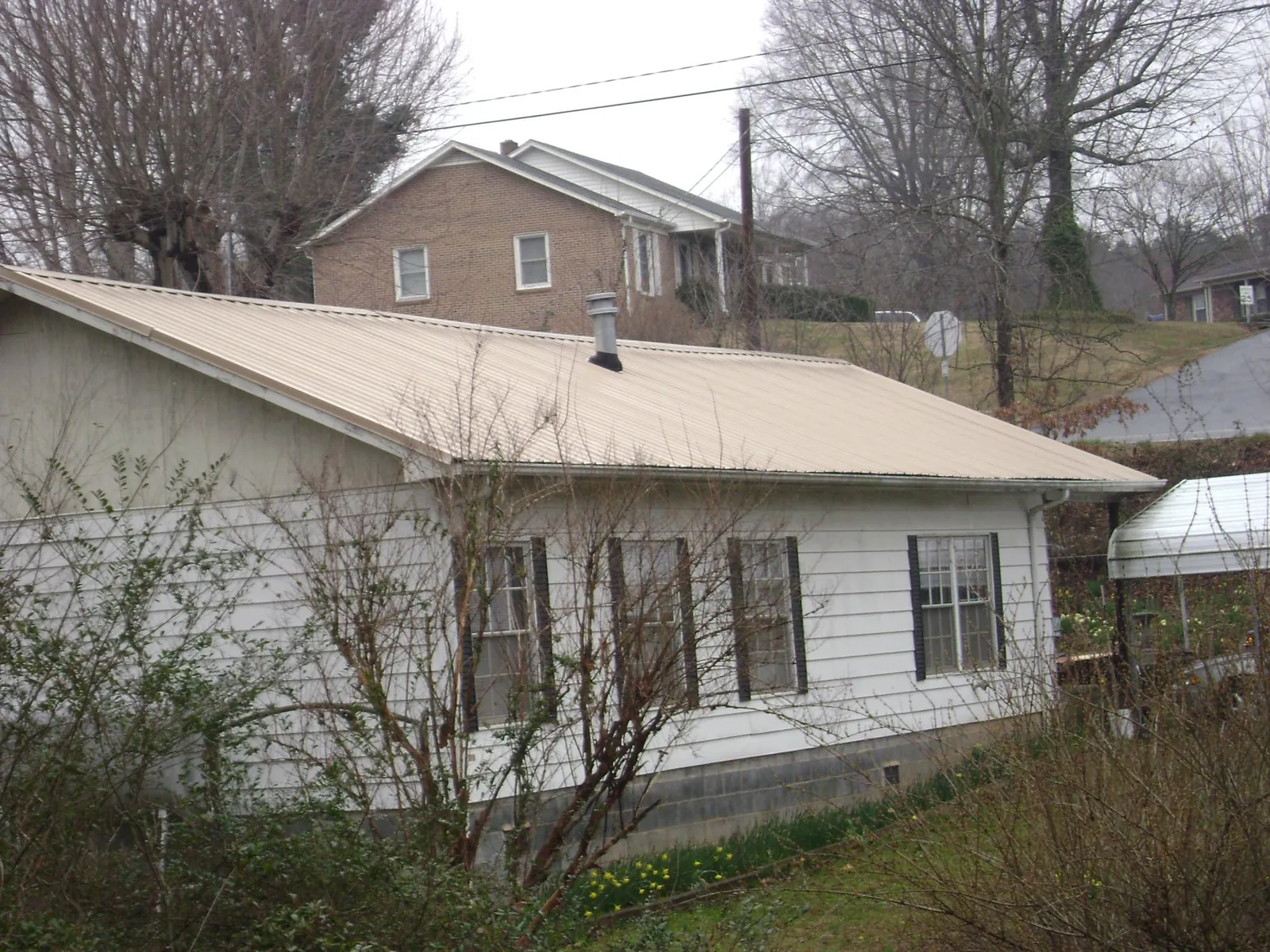 Tan metal roof on a white sided house set into a hillside — Commercial Roofing by Roofing Brothers in Staples
