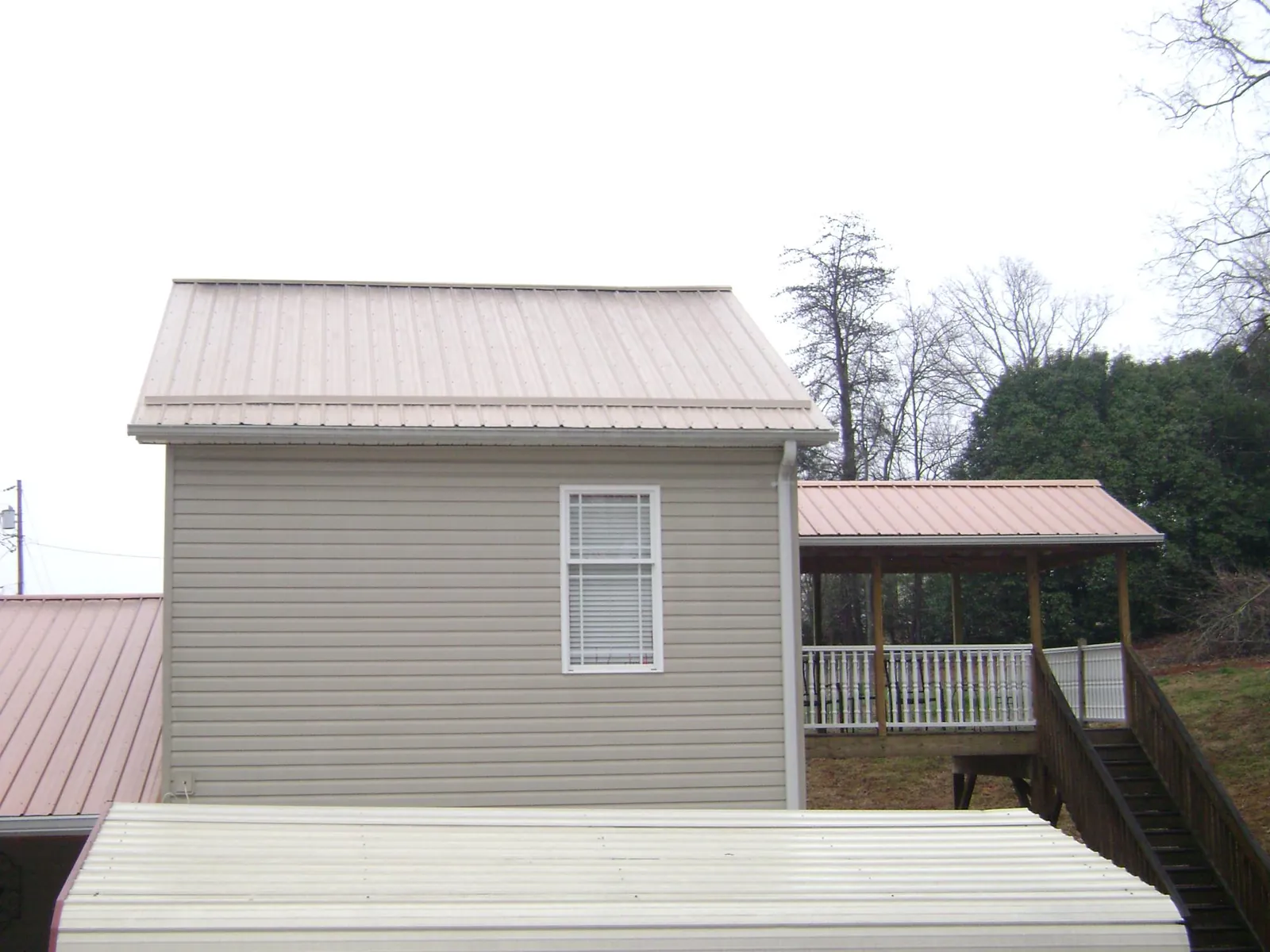 Tan metal roofs on a two story addition and attached porch, from a Roof Replacement job in Staples